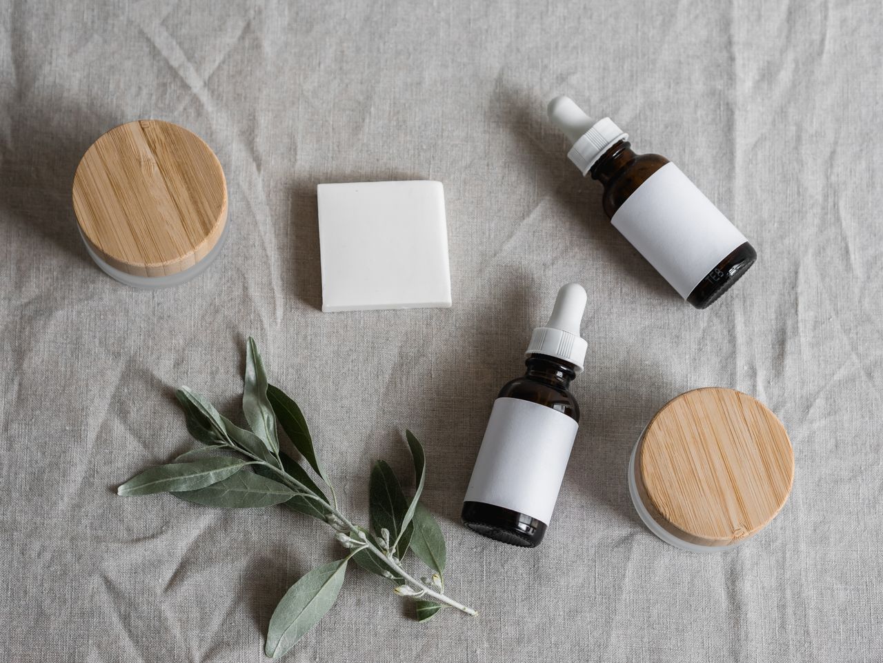 About Top view of skincare products with a natural theme, featuring bottles, jars, and a plant on linen cloth.